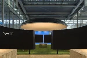 Modern art gallery with a blue floor, black ceiling, and a large window, featuring a display of artwork in a well-lit space
