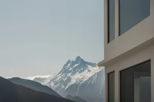 A modern building with a concrete exterior, set against a blue sky with a snow-covered mountain in the background