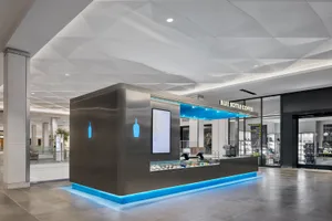 A modern coffee shop with a predominantly black interior, blue accents, and a large window for natural light, featuring a counter with a display of bottles