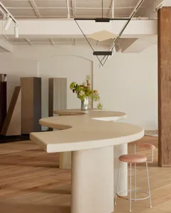 Modern kitchen with a large marble island, a sink, a vase with flowers, and a potted plant, set against a clean and minimalistic backdrop