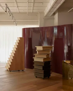 Cozy study with a purple accent wall, wooden floor, and a large bookshelf with various books, natural light from a window