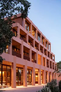 Large modern building with a pink concrete facade, numerous windows, and a warm inviting atmosphere