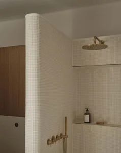 A well-lit bathroom with a white tile wall, a gold shower head, and a bottle on the wall, creating a modern and luxurious atmosphere