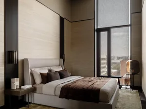 A modern bedroom with a wooden floor, a brown wall, and a bed covered in a brown blanket with pillows, near a window with natural light