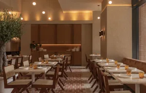 Warm and inviting dining space with tables, chairs, orange napkins, and wine glasses, featuring a combination of wood and brick elements