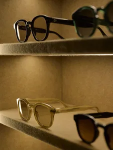 A store display area with a wooden shelf showcasing various metal glasses in different positions, set against a soft and diffused background