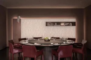Dining room with a round table set with wine glasses, bowls, and vases, surrounded by chairs, and a couch in the background, featuring wood and marble materials