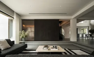A modern living room with a black wall, wooden table, and vase with flowers, featuring a couch and chair, with natural light from a window