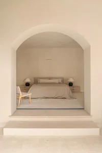 A cozy bedroom with a bed, chair, and lamp, featuring wood and fabric materials, soft lighting, and a focus on relaxation