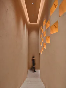 A calm and quiet hallway with a person walking towards the camera, surrounded by pictures on the wall in a residential building made of concrete
