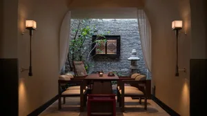 A modern dining room with a wooden table and chairs, surrounded by a brick wall, with a vase on the table, in a dimly lit space