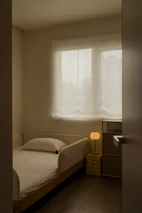 柔和的臥室，有一張床、夜櫃和敞開的窗戶，靠近夜櫃放著一盞黃色燈泡