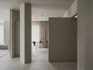 A dimly lit dining area with a wooden table and chairs, surrounded by metal elements in a predominantly white space