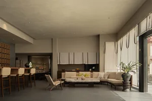 Comfortable and inviting living space with a large couch, chair, dining table, and decorative elements, featuring a large window with natural light and soft warm lighting
