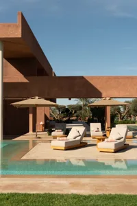 A relaxing outdoor pool area with a patio, furniture, and umbrellas, surrounded by natural materials and providing shade and a warm ambiance