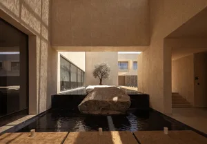 A large, modern lobby with a central pool of water surrounded by rock and potted plants, featuring marble and glass materials and a sense of calm and luxury