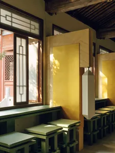 A modern restaurant with a yellow and green color scheme, featuring wood furniture and large windows for natural light