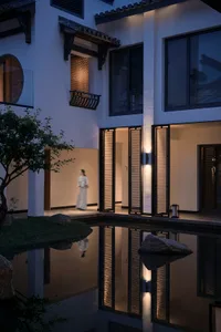A woman walks in front of a modern building with a reflecting pool in a serene courtyard setting