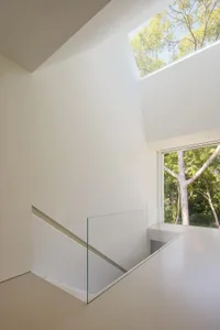 White staircase with a glass railing in a modern minimalist room with a nearby window