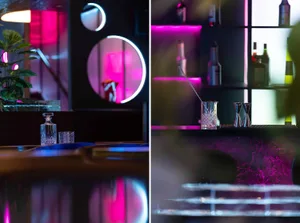 A modern bar scene with pink lighting, bottles, and glasses on the counter and around the bar area, creating a warm and inviting atmosphere