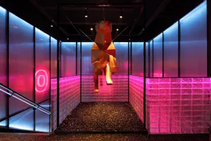 A modern room with a pink and black color scheme, featuring a staircase with a pink railing, a red wooden horse sculpture hanging from the ceiling, and a unique artistic touch