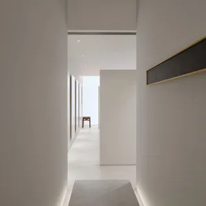 A dimly lit hallway with white walls, a wooden floor, and a single chair, creating a minimalist and clean atmosphere