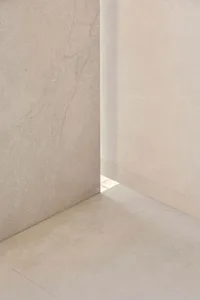 A minimalist room with a concrete wall and white floor, lit by natural sunlight through a window