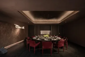 Dining room with a round table, red chairs, wooden floor, and brown color scheme, set with plates, bowls, and wine glasses, with dim lighting