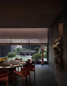 Cozy dining space with a round table, chairs, and potted plants, set with plates, wine glasses, and bowls, in a dimly lit modern room