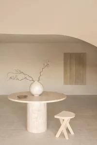 A minimalist dining area with a white table, a ceramic vase, and a couch and chair, surrounded by soft and diffused lighting