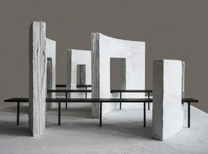 A modern stone building with a concrete floor, featuring a large stone wall and a stone bench, bathed in natural light from the sun