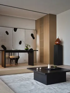 A modern living room with a black coffee table, chair, and table, decorated with a potted plant and vase, under warm and inviting lighting