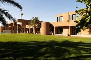 A modern house with a brown exterior, surrounded by palm trees and a lush green lawn, with natural light and a clean design