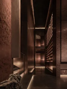 A dimly lit hallway with a stone floor and walls, featuring a staircase and doorway, in a mix of residential and commercial style