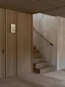 A dimly lit hallway with a wooden staircase and door, surrounded by a wall on one side and a door on the other