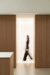 A woman in a black dress walks towards a sink in a kitchen with a wooden floor and a white door