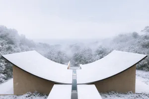 A modern building with a curved structure is set against a serene snow-covered landscape