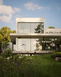 A modern house with a white exterior, glass wall, and lush green surroundings, featuring a clean and minimalistic design