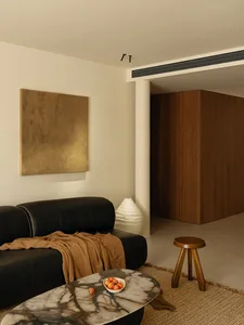 Cozy living room with a black couch, chair, and dining table, featuring a white wall, brown wooden door, and decorative elements