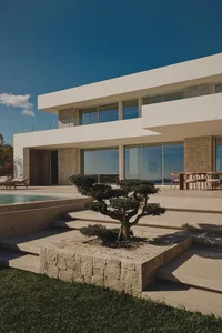 A large modern house with a pool and patio, surrounded by white materials and well-lit for a bright and inviting atmosphere