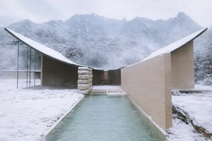 A modern house with a central swimming pool surrounded by a stone wall, set in a snowy winter landscape