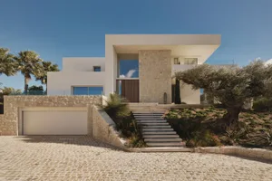 Large white house with a stone exterior, surrounded by lush greenery and a spacious interior with natural light from a large window