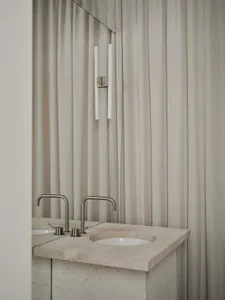 Bathroom with a marble sink under a white curtain, a mirror above, and a white color scheme, lit by natural light