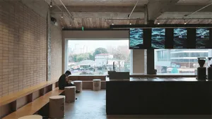 A dark and moody restaurant living space with a bar, dining table, and TVs, featuring a man sitting on a bench