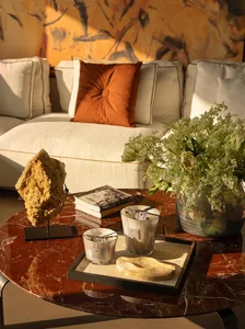 A modern living room with a couch, coffee table, and vase with flowers, featuring marble and wood materials and bright, inviting lighting