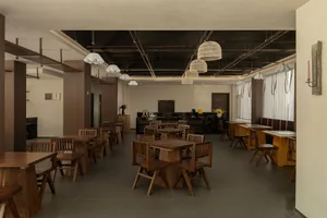 A modern restaurant with a large dining area featuring wooden tables and chairs, well-lit to create a warm and inviting atmosphere