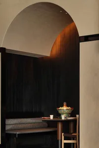 Cozy dining space with a wooden table, bench, and warm wooden wall, set with cups and bowls, in a dimly lit room