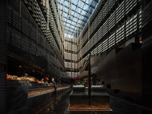 A dimly lit, modern commercial space with glass and metal surfaces, featuring potted plants near windows