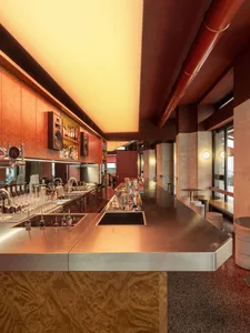 Modern bar area with a metal counter, wooden floor, and well-lit space with bottles on the counter