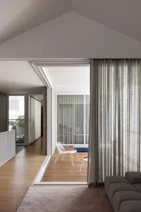 Modern living room with a wooden floor, glass door, chair, couch, and dining table, well-lit with natural light